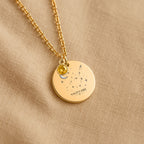 Détail de la médaille constellation Sagittaire et de sa chaîne sur un tissu beige