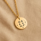 Détail de la médaille Signature Astrale et de sa chaîne sur un tissu beige