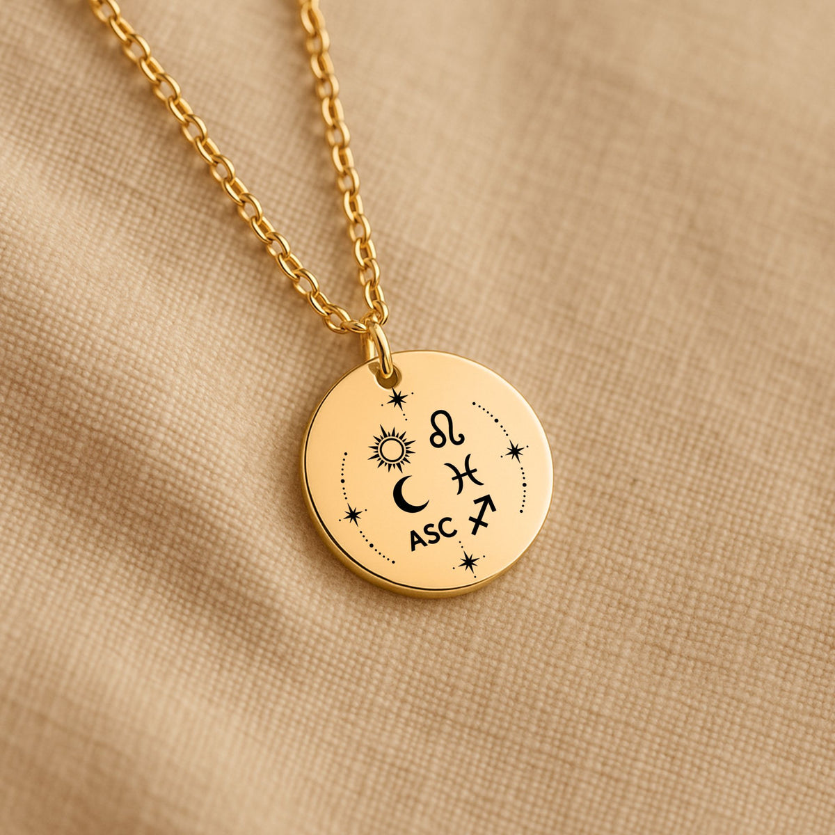 Détail de la médaille Signature Astrale et de sa chaîne sur un tissu beige