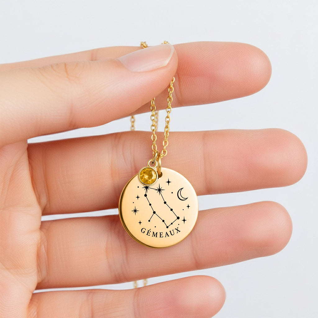 Collier constellation Gémeaux tenu entre les doigts, médaille ronde gravée et pierre de naissance