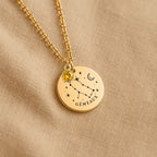 Détail de la médaille constellation Gémeaux et de sa chaîne sur un tissu beige
