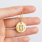 Collier Signature Astrale tenu entre les doigts, médaille gravée Soleil, Lune et Ascendant