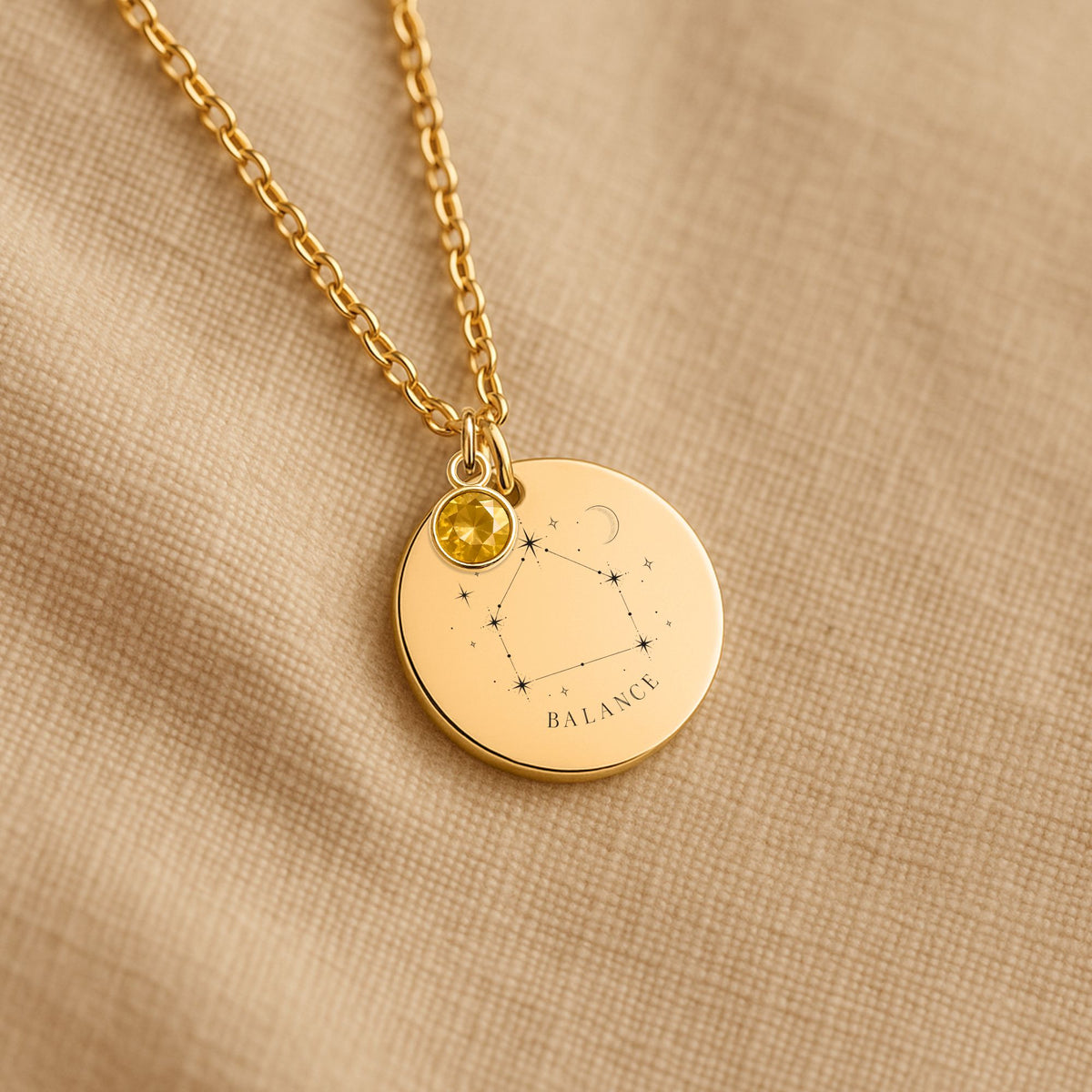 Détail de la médaille constellation Balance et de sa chaîne sur un tissu beige