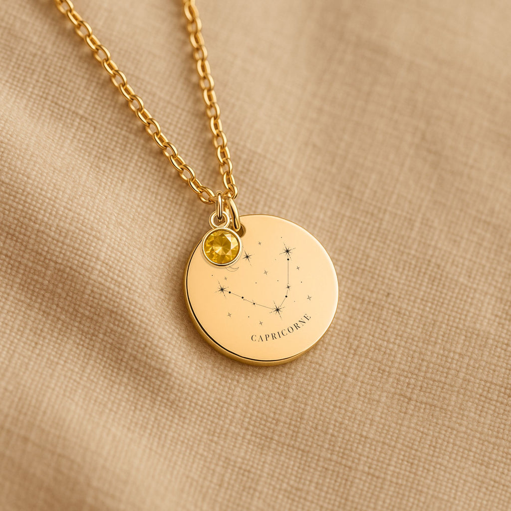 Détail de la médaille constellation Capricorne et de sa chaîne sur un tissu beige