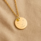 Détail de la médaille constellation Capricorne et de sa chaîne sur un tissu beige