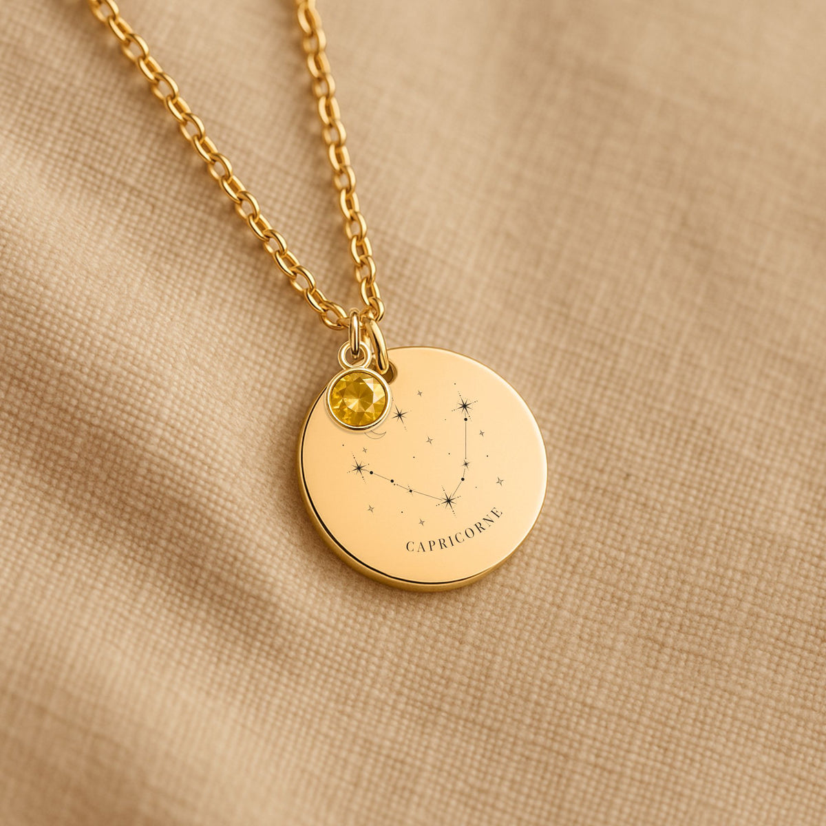 Détail de la médaille constellation Capricorne et de sa chaîne sur un tissu beige